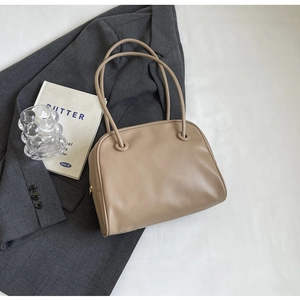 Close-up of beige minimalist tote bag with long cylindrical handles and gold zipper