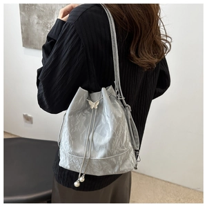 Sac seau argenté métallisé avec boucle papillon et détails de perles porté à l'épaule