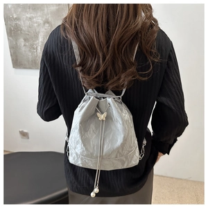 Détail du sac à dos seau gris clair avec papillon doré et accents de perles blanches