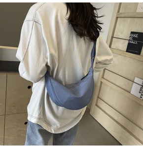 Mannequin portant un sac bandoulière demi-lune en nylon bleu en intérieur épuré