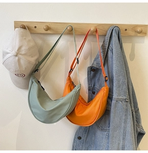 Détail de sacs demi-lune en nylon vert menthe et orange sur un cintre avec habits