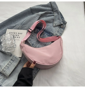 Sac bandoulière demi-lune en nylon rose posé sur une veste en jean avec accessoires
