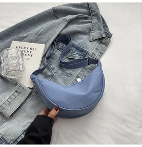 Détail d'un sac bandoulière en nylon bleu en forme de croissant sur une veste en jean