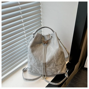 Détail du sac seau argenté texturé avec cordon, papillon en métal et breloques en perles