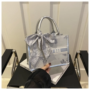 Détail d'un sac cabas argenté avec un nœud en soie paisley bleu et logo texte