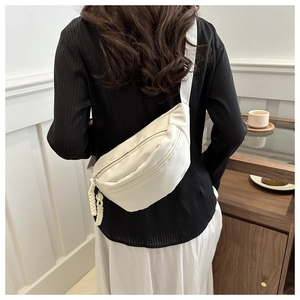 Detail of a creamy white versatile chest bag with woven zipper pull on a stylish model