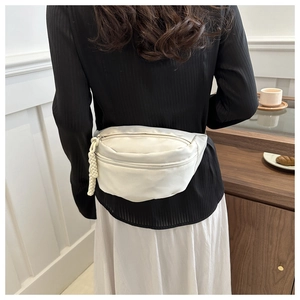 Minimalist beige crossbody waist bag worn over a striped shirt in a cafe setting