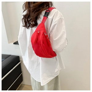 Detail of red nylon crossbody bag with dual zippers and woven cord pullers on a model