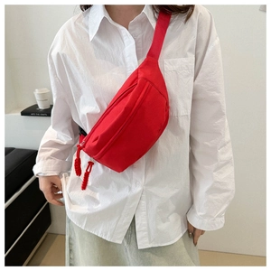 Detail of red crossbody chest bag featuring woven zipper pulls and wide shoulder strap