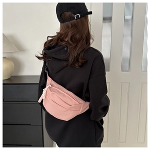 Detail of pink nylon crossbody chest bag worn over a black hoodie in a modern home setting