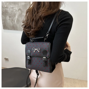 Rear view of a model wearing the dark grey backpack with red heart patterns and bow detail