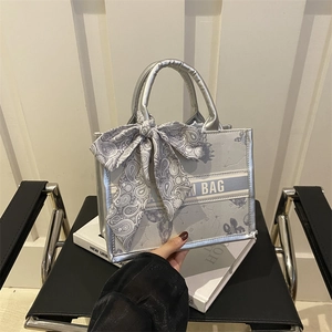 Sac cabas en toile argentée avec lettrage et nœud en soie fleurie sur une chaise noire