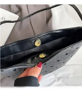 Detail of grey polka dot woven bag with black leather trim and golden magnetic closure