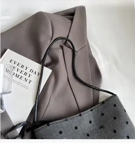 Detail of grey wool bucket bag with black polka dots, embroidery, and silk bow detail