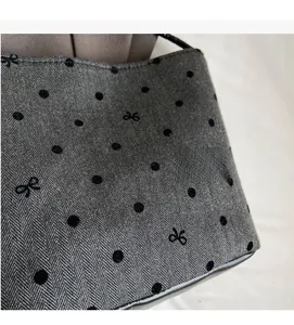 Close-up of grey herringbone fabric with black polka dots and bow embroidery details