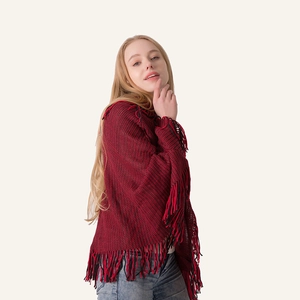 Detail of red and black knit poncho with tassel fringe and V-shaped hemline