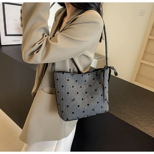 Detail of grey hobo bag featuring embroidered black polka dots and a side ribbon bow