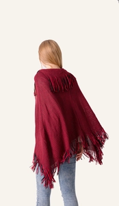 Detail view of red and black knit poncho featuring thick texture and fringed hemline