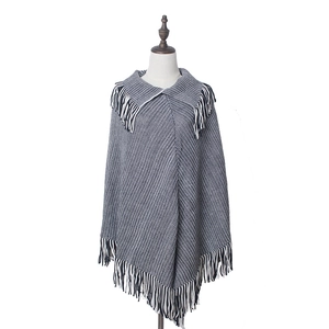 Detail of knit poncho featuring large lapel collar and long fringe hem in black and white