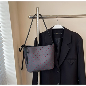 Detail of grey shoulder bag with red heart patterns and black ribbon on a hanger