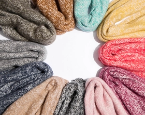 Detailed overhead view showing various colorful chunky knit scarves with fringe tassels