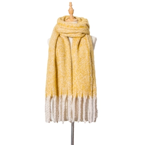Macro detail of thick yellow and white knit scarf featuring chunky braided tassels