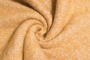 Macro detail of camel yellow knitted scarf showing soft texture and twisted fabric rolls