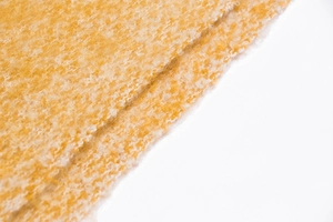 Detailed close-up of thick bouclé yarn texture in ginger yellow and white knit scarf