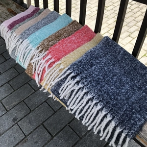 Detail of colorful knitted scarves with thick fringe tassels on a wooden surface