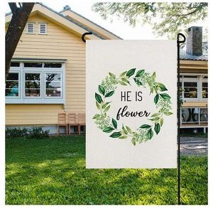 Detail of a white garden flag with green wreath and HE IS text on a black metal pole