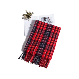Flat lay of red and black checkered scarf with tassels next to lifestyle props
