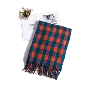 Detail of orange and teal checkered scarf with long tassels beside dried flowers