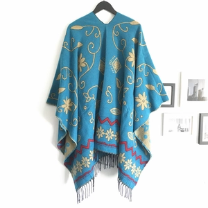 Detail of dark blue ethnic knit shawl with golden floral patterns and black fringe trim