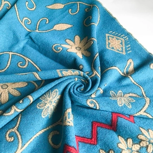 Ethnic blue knit shawl with sunflowers and vine patterns in a spiral fold arrangement
