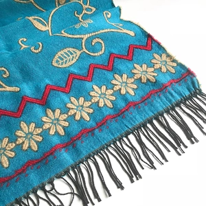 Ethnic knit shawl featuring sunflower embroidery, peacock blue base, and black fringe trim