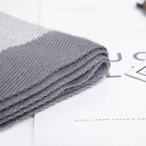 Detail of grey knitted scarf with textured ribbing and striped pattern on white background