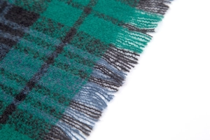 Detailed close-up of green plaid poncho fabric with handcrafted fringe tassels
