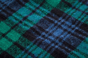 Close-up of green and blue plaid wool fabric showing the detailed brushed texture of the cloak