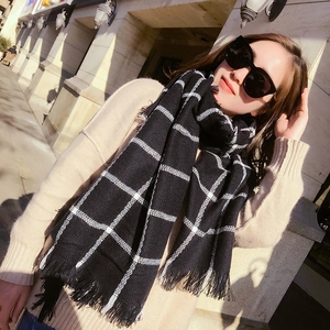 Outdoor model wearing a large black and white plaid scarf with fringe in autumn sunlight