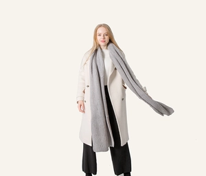 Grey long knit scarf with coarse ribbed texture worn by a model in a white coat