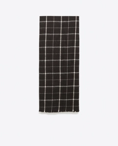 Detailed view of the black and white plaid scarf featuring classic fringe tassels at edges