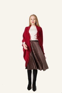 Détail d'un poncho en tricot rouge à franges porté avec une jupe longue plissée