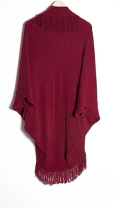 Détail d'un poncho en maille bordeaux avec des franges denses et des manches chauve-souris