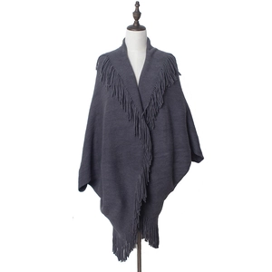 Détail d'un poncho en maille gris foncé avec des franges épaisses sur le bord et le col