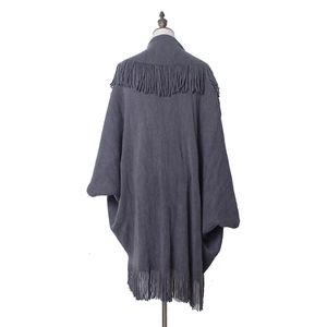 Détail d'un poncho en tricot gris foncé avec d'élégantes franges longues sur l'ourlet