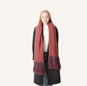 Close-up of a warm winter knit scarf with dark red fabric and long purple tassels