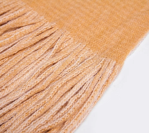 Macro detail of the ginger yellow knitted scarf showing warm texture and long fringe edges