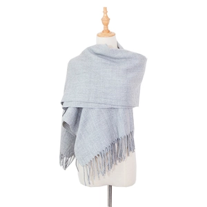 Detail view of light grey cashmere-like scarf with soft long tassels on a model