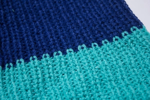 Macro detail of ribbed knit fabric showing teal and navy blue color block stitching