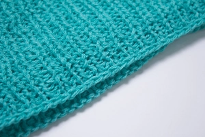 Close-up of teal knitted scarf showing intricate hollow stitch patterns and soft wool texture